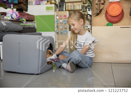 Portrait of cute little girl and dog sitting in new soft house at pet shop 121223752