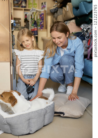 Happy mother and daughter watching dog testing new sleeping bed at pet store 121223765