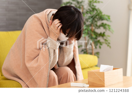 A middle-aged to senior woman wearing a mask suffering from a headache in a winter room A middle-aged to senior woman wearing a mask suffering from a headache in a winter room 121224388