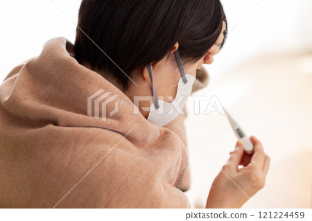 A middle-aged to senior woman wearing a mask suffering from a headache in a winter room A middle-aged to senior woman wearing a mask suffering from a headache in a winter room 121224459