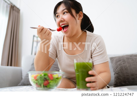 Beautiful Asian woman eating salad, holding a glass bowl and using a fork to pick up a tomato to eat Beautiful Asian woman eating salad, holding a glass bowl and using a fork to pick up a tomato to eat 121224747