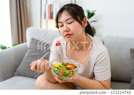 An Asian fat woman feels bad and bored while eating a salad. She doesn't like to eat vegetables. An Asian fat woman feels bad and bored while eating a salad. She doesn't like to eat vegetables. 121224748
