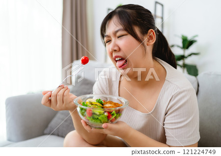 An Asian fat woman feels bad and bored while eating a salad. She doesn't like to eat vegetables. 121224749