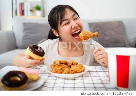 A beautiful Asian woman eats fried chicken and donuts with a smile on her face. A beautiful Asian woman eats fried chicken and donuts with a smile on her face. 121224753
