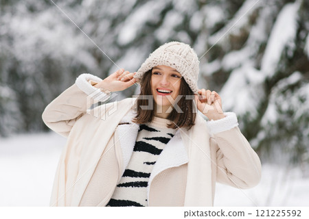 Young happy woman wearing beige hat and striped sweater is smiling in the snow Young happy woman wearing beige hat and striped sweater is smiling in the snow 121225592