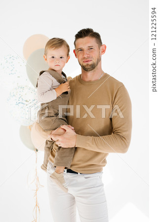 Father holds his son in his arms, holding a bunch of balloons in his hands against the background. Scene turned out to be carefree and playful, festive 121225594
