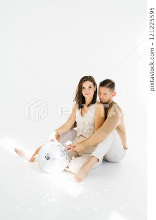 Couple is sitting on the floor with a disco ball in front of them. Scene is playful and fun Couple is sitting on the floor with a disco ball in front of them. Scene is playful and fun 121225595