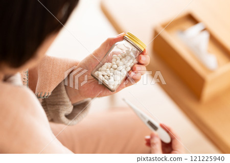 Middle-aged to senior women holding pills and a thermometer 121225940