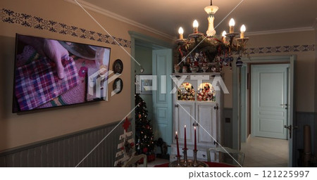 A cozy kitchen decorated for Christmas features a table with candles and a beautifully adorned tree, while a screen shows festive crafting activities. Festive Christmas kitchen interior decor A cozy kitchen decorated for Christmas features a table with candles and a beautifully adorned tree, while a screen shows festive crafting activities. Festive Christmas kitchen interior decor 121225997