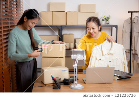 Two young asian woman live online clothing store while showing clothing with tablet and laptop. Two young asian woman live online clothing store while showing clothing with tablet and laptop. 121226726