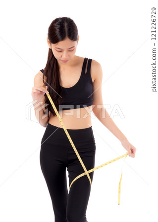 Portrait young asian woman in sportswear holding measuring tape leg for weight loss isolated. 121226729