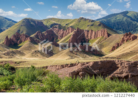 Stunning red rock formations majestically rise amidst the lush green mountains, showcasing natures incredible beauty of Kazakhstan, Almaty region. 121227440