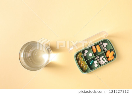 Pill box with various pills and vitamins and a glass of water, top view, copy space. 121227512