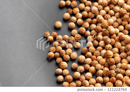 Dried coriander seeds with textured brown shells scattered on a dark surface. Aromatic spice for culinary use. Close-up. Top view. 121228760