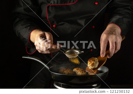 A chef expertly seasons meatballs with paprika in a dark kitchen, focusing on perfecting the flavour. European cuisine 121230132