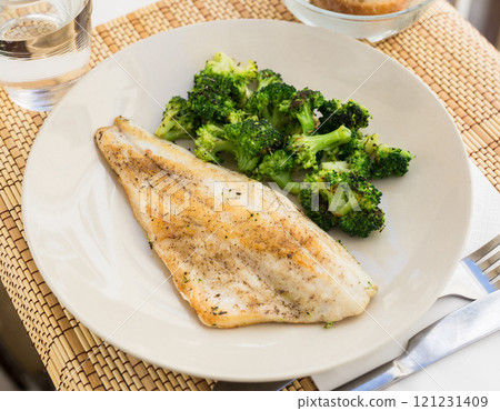 Fried fillet of sea bass with garnish of broccoli on black warm stone plate Fried fillet of sea bass with garnish of broccoli on black warm stone plate 121231409