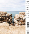 Coastal scene showcasing a rugged cliff split into two sections, revealing the ocean in the background. 121233291