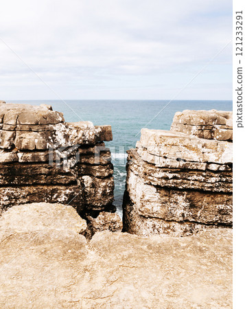 Coastal scene showcasing a rugged cliff split into two sections, revealing the ocean in the background. 121233291