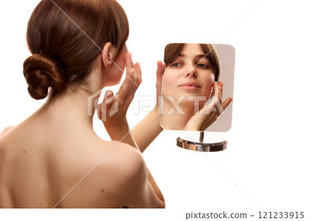 Back view image of young beautiful woman holding mirror and applying face moisturizing cream against white studio background Back view image of young beautiful woman holding mirror and applying face moisturizing cream against white studio background 121233915