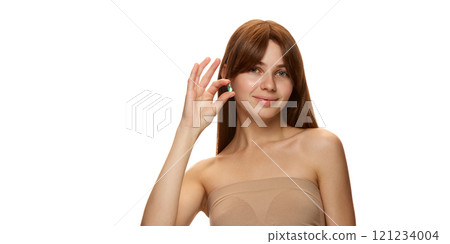 Smiling young woman holding green serum capsule for hair and head skin treatment against white studio background 121234004