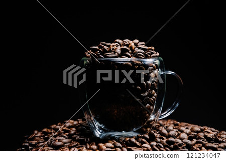 Roasted coffee beans overflowing a glass cup on a black background 121234047