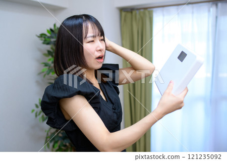 Woman holding a weight scale and holding her head, regret, weight concern, diet, shock 121235092