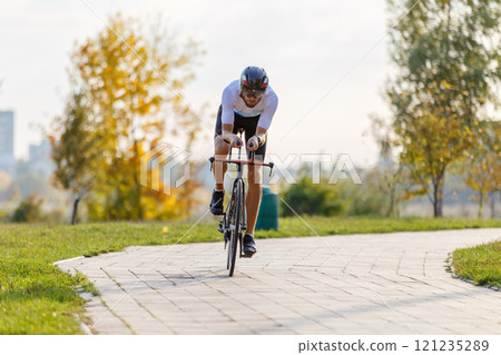 Cyclist riding on a pathway surrounded by autumn foliage in a park Cyclist riding on a pathway surrounded by autumn foliage in a park 121235289