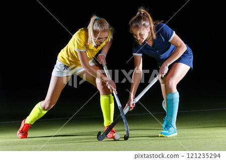 Two female hockey players competing in an intense match in contrast light Two female hockey players competing in an intense match in contrast light 121235294