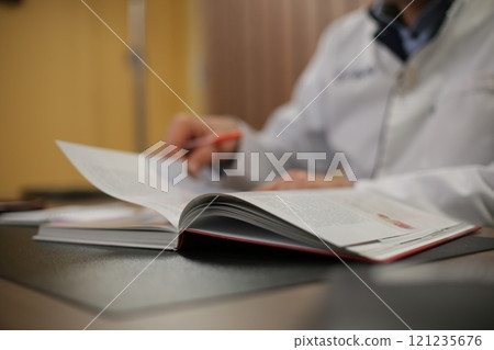A diligent doctor is sitting at a desk, deeply focused on reading a book A diligent doctor is sitting at a desk, deeply focused on reading a book 121235676
