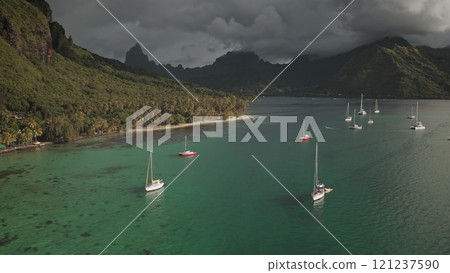 Many sailboats yachts stop in turquoise, shallow water of Opunohu bay, Moorea, French Polynesia, green mountains and palm trees under dramatic cloudy sky. Wild nature paradise, exotic summer travel 121237590