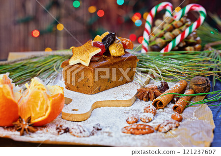 Christmas fruit cake garnished with marzipan star, dried fruits, and nuts, surrounded by spices, oranges, and pine branches on rustic table 121237607