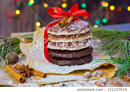 Stack of iced and chocolate-dipped gingerbread cookies tied with red ribbon and topped with cinnamon sticks. Festive holiday decorations Stack of iced and chocolate-dipped gingerbread cookies tied with red ribbon and topped with cinnamon sticks. Festive holiday decorations 121237610
