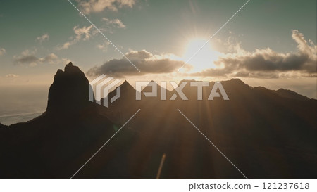 Golden sunbeams illuminate jagged volcanic mountain peaks on Moorea tropical island in French Polynesia, creating a breathtaking aerial view of paradise sunset. Wild nature popular tourist destination 121237618
