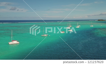 Aerial drone view of sailboats yachts and catamarans moored in shallow, turquoise water near a tropical island, creating a serene and idyllic scene, relaxing summer holiday vacation or getaway concept 121237620
