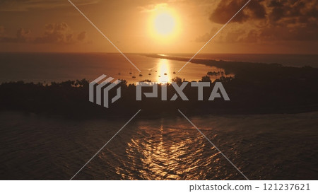 Golden sunrise illuminate yachts anchored near tropical island with lush vegetation in Rangiroa, French Polynesia, breathtaking sky seascape. Remote wild nature paradise, exotic summer travel. Aerial 121237621