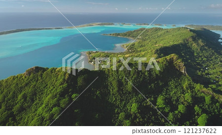Aerial drone captures the breathtaking beauty of Bora Bora mountains, tropical island in French Polynesia, where lush green vegetation covers volcanic slopes meeting a vibrant turquoise lagoon 121237622