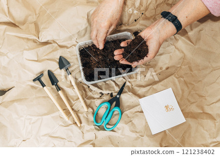 Kraft paper background, fertile soil and garden tools, top view. Hands planting seeds 121238402