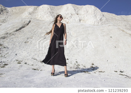 A beautiful girl in a black long dress stands against the background of chalk mountains. 121239293