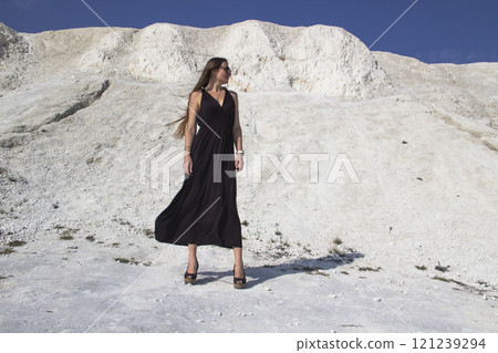 A beautiful girl in a black long dress stands against the background of chalk mountains. 121239294
