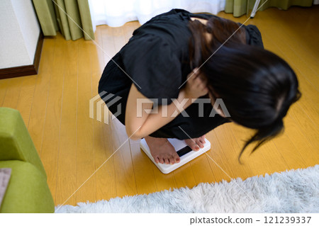 Woman weighing herself, looking at the scale, worried about her weight, diet Woman weighing herself, looking at the scale, worried about her weight, diet 121239337