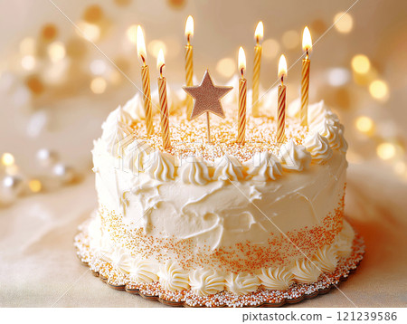 Elegant white birthday cake with lit golden candles and a sparkling star topper 121239586