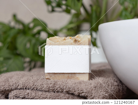 Soap bar with blank label on brown folded towel near plant and basin in bathroom, mockup 121240167