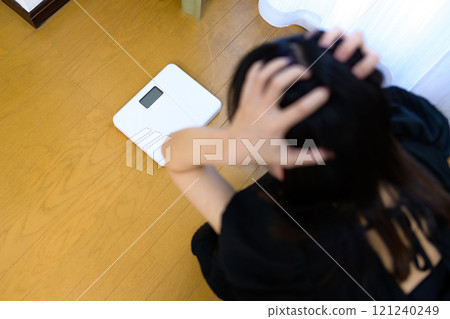 一個女人稱體重，看著體重秤，抱著頭，擔心自己的體重，節食 121240249