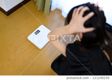 一個女人稱體重，看著體重秤，抱著頭，擔心自己的體重，節食 121240250