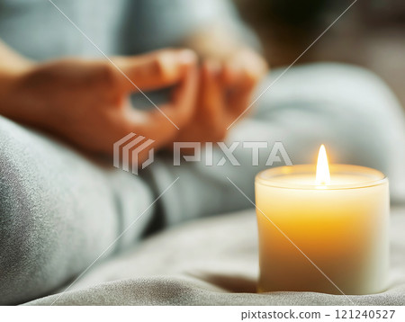 A serene scene featuring a lit candle in the foreground, with a blurred figure in a meditative pose 121240527