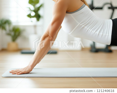 Woman in activewear performing a plank exercise on a yoga mat in a bright living room 121240618