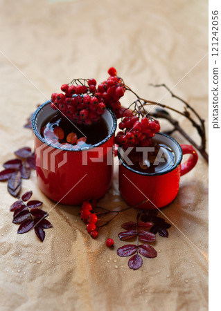 two red mugs with tea, a branch of autumn rowan lies nearby 121242056