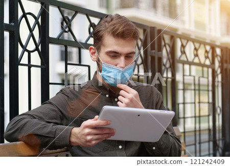 Young businessman in protective mask read online newspaper via tablet computer Young businessman in protective mask read online newspaper via tablet computer 121242409