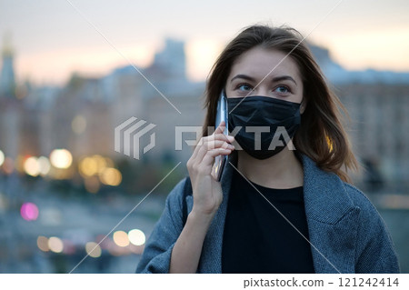 Young girl in medical protective face mask speaks on smartphone Young girl in medical protective face mask speaks on smartphone 121242414