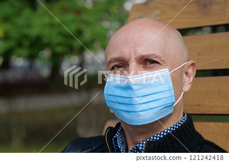 Bald senior man in medical protective face mask looks at the camera 121242418